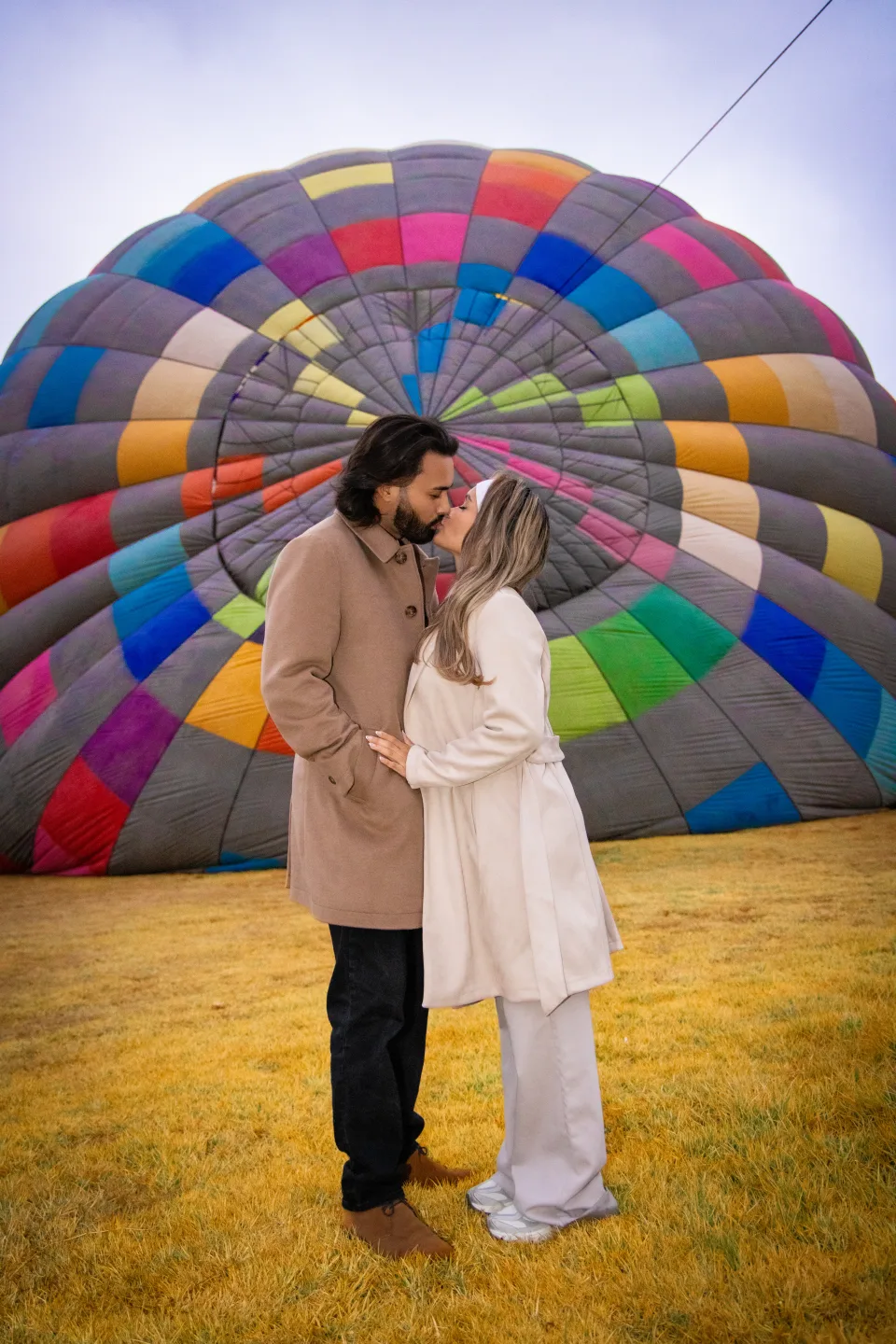 Couple about to kiss in front of a colorful hot air balloon on the field