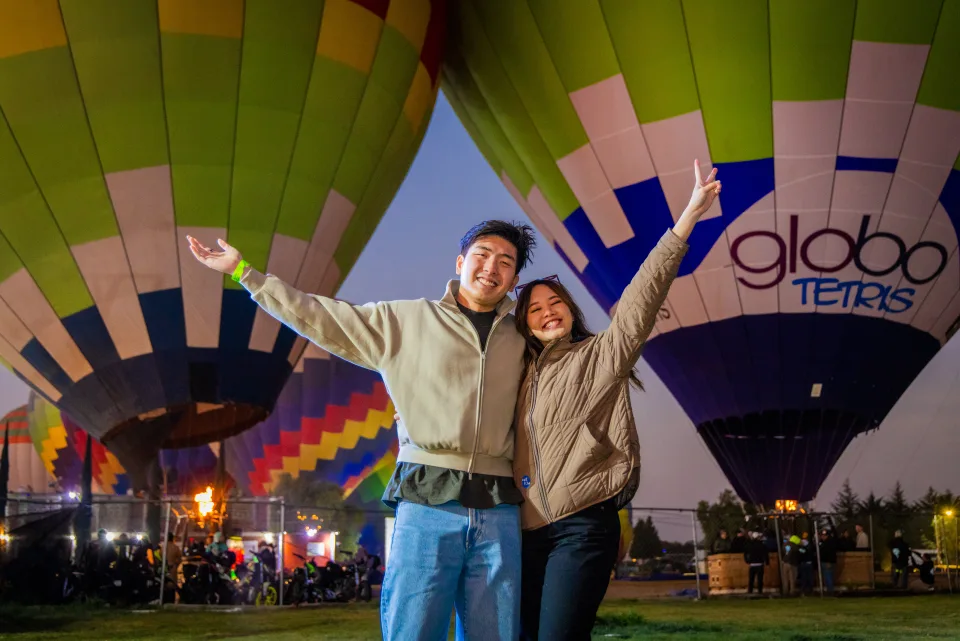 Excited couple with arms raised before glowing hot air balloons before dawn