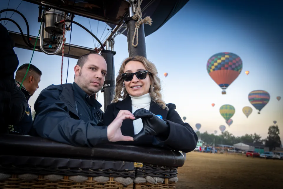 Couple forming a heart with their hands inside a hot air balloon basket at sunrise