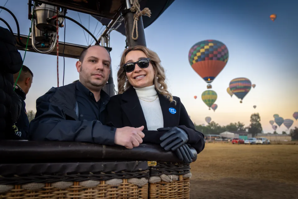 Couple inside a balloon basket with many balloons rising at sunrise