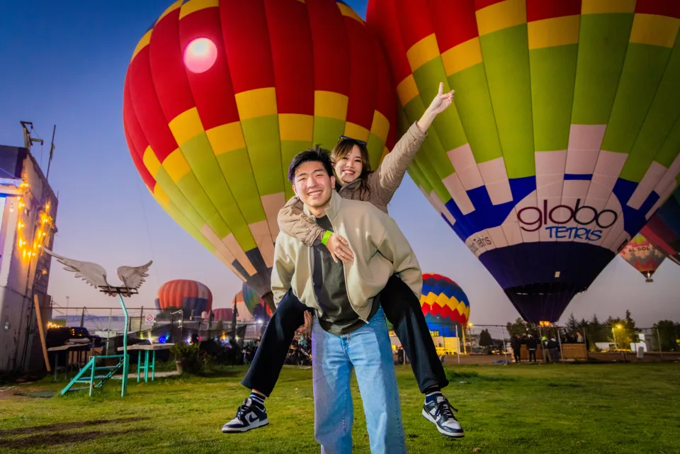 Couple piggyback riding with vivid glowing hot air balloons and fairy lights at dawn