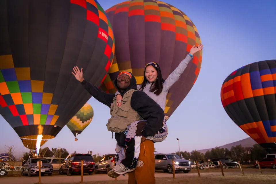Couple piggyback riding with hot air balloons around them at sunrise