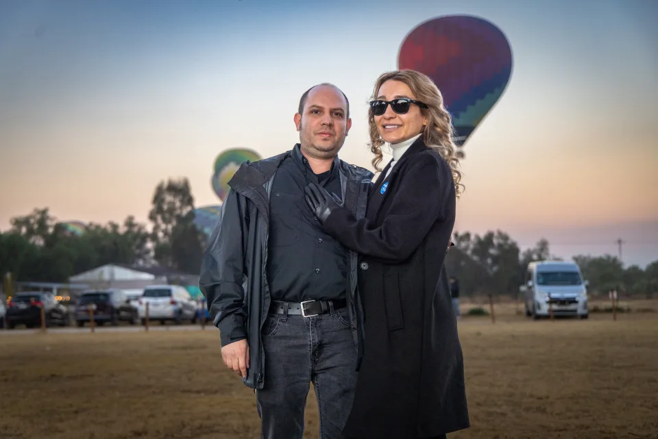 Couple posing together with hot air balloons and the sunrise sky behind them