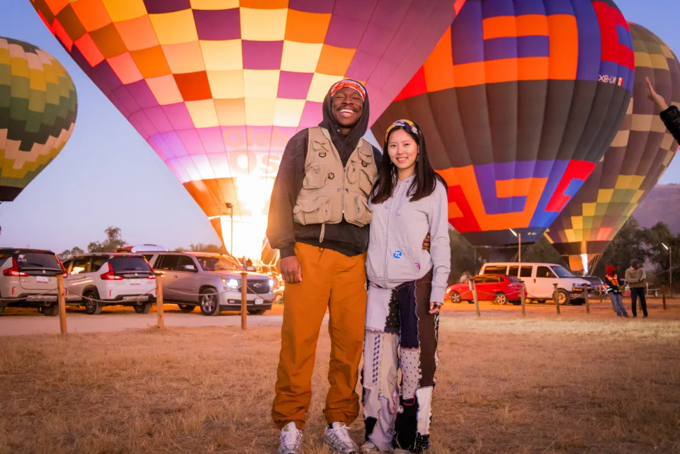 Couple posing together before glowing hot air balloons at sunrise in the launch field
