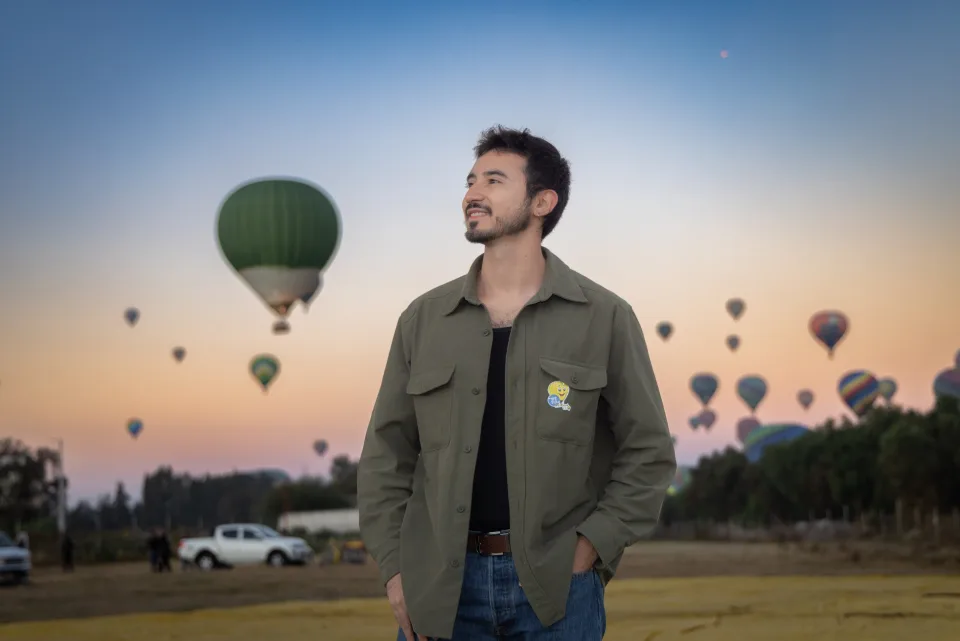 Man standing in the field as many hot air balloons drift across the sunrise sky over Teotihuacan