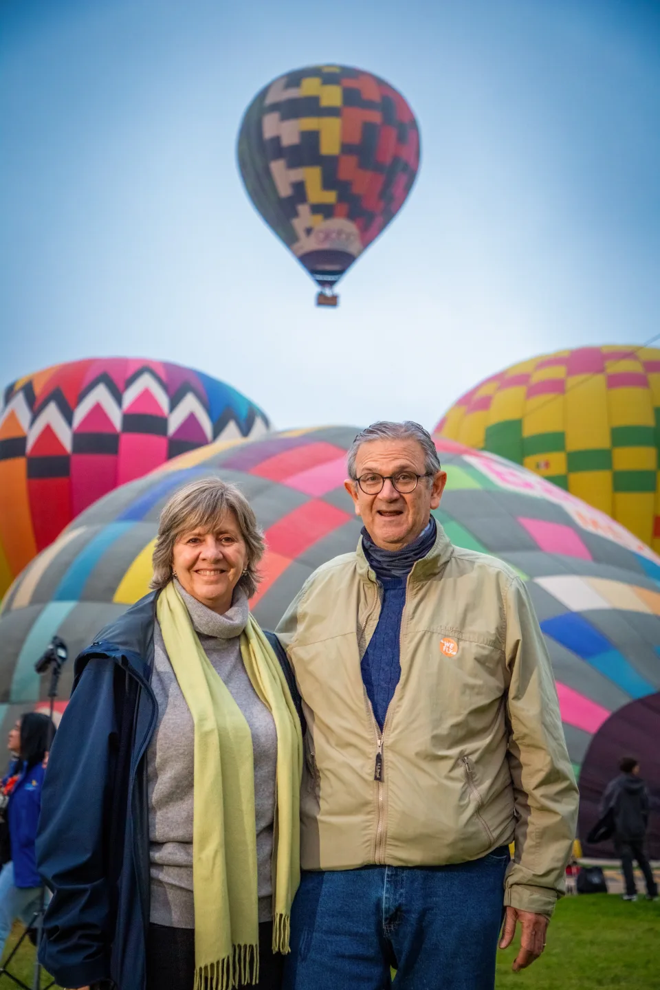 Smiling older couple with colorful hot air balloons inflating behind them at sunrise