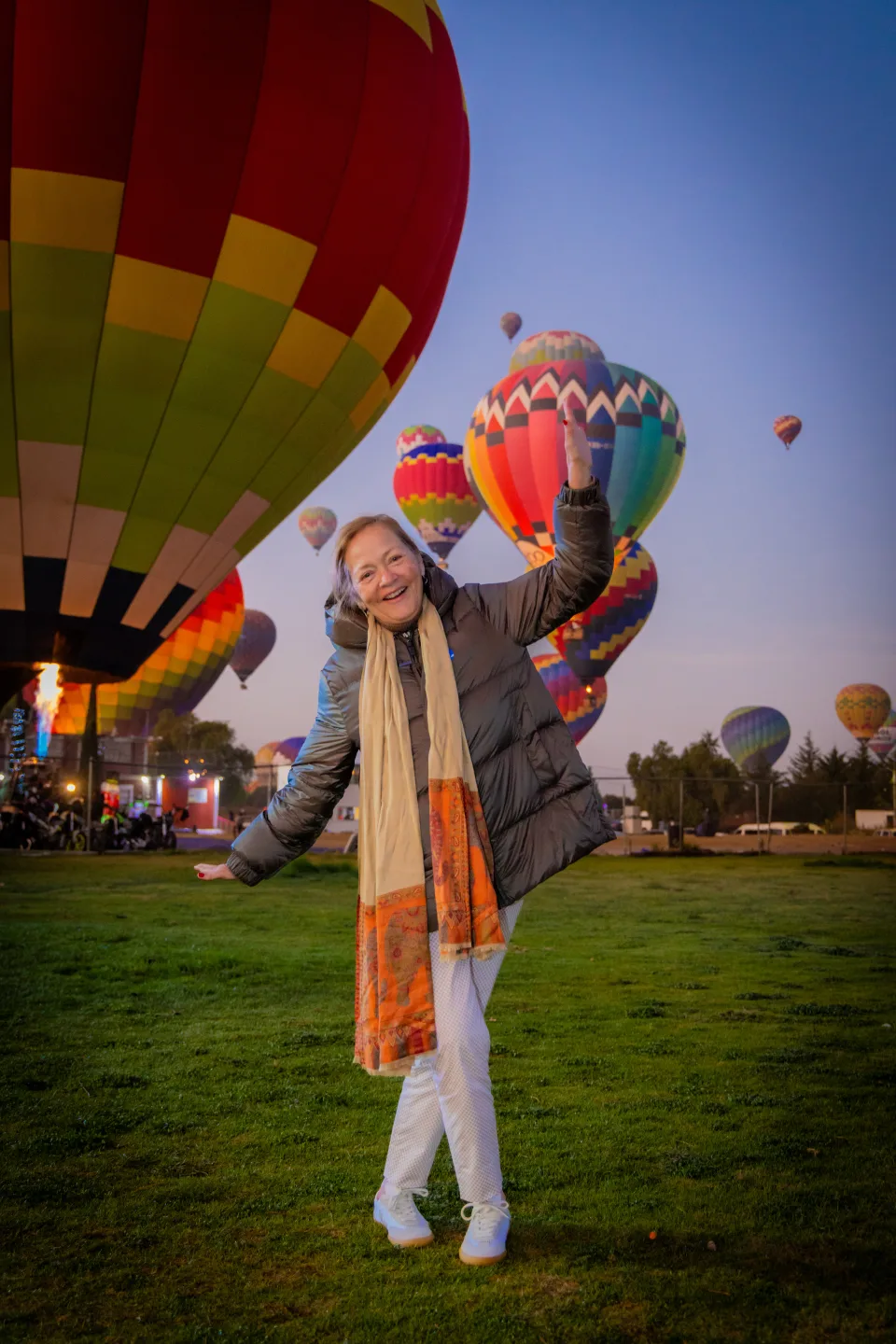 Cheerful older woman posing playfully with many balloons at sunrise