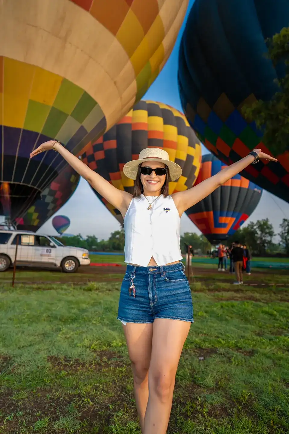 Viajera con sombrero abre los brazos frente a tres globos aerostáticos inflados al amanecer en Teotihuacán