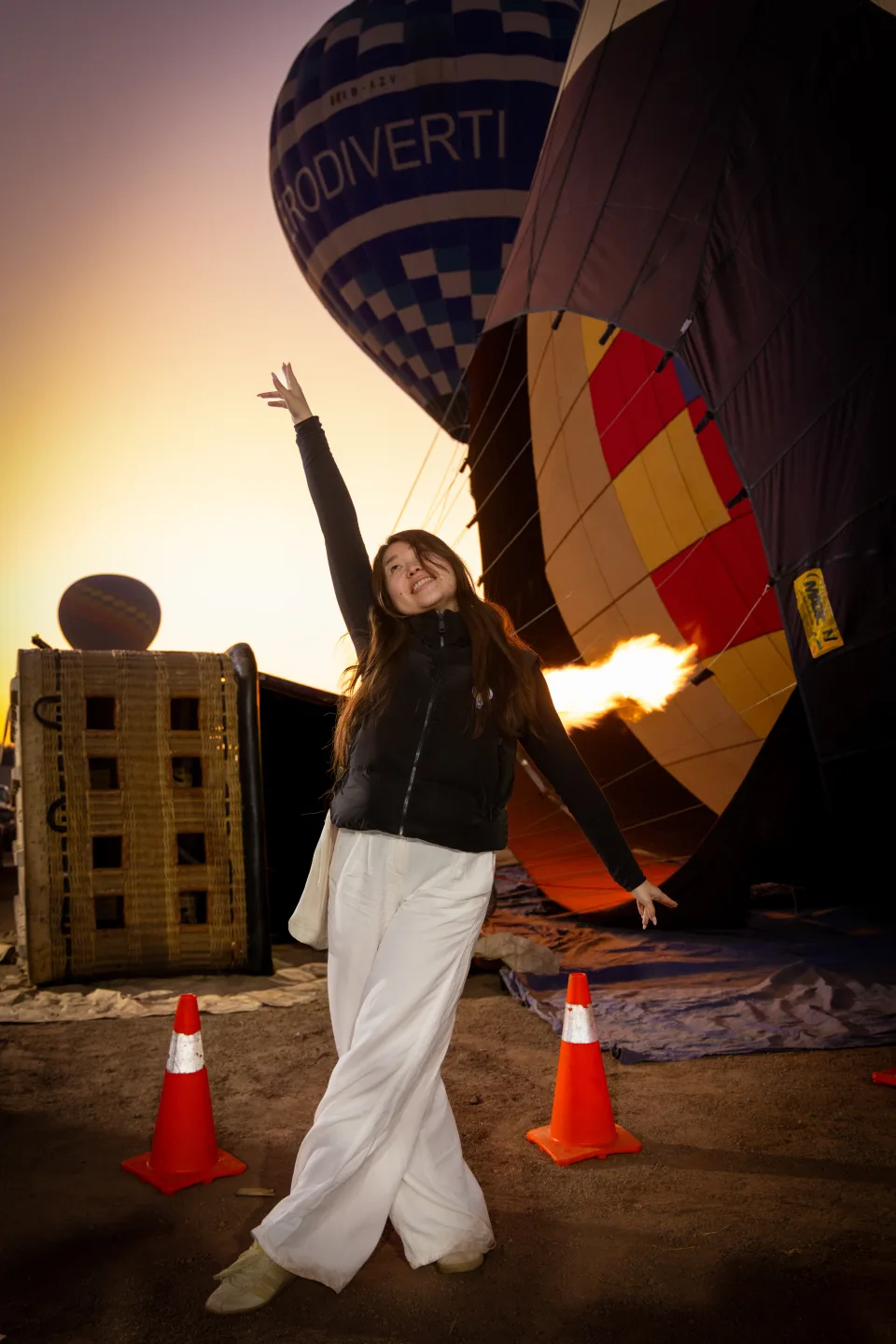 Young woman with arms raised against a golden sunrise as the burner fires