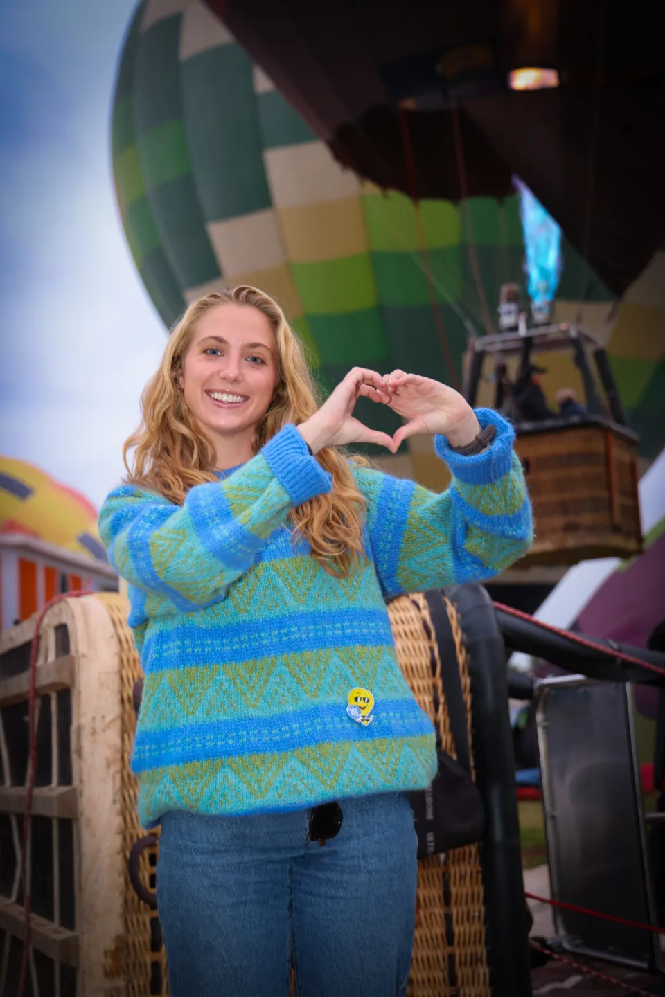 Young woman forming a heart with her hands beside a hot air balloon at dawn in Teotihuacan