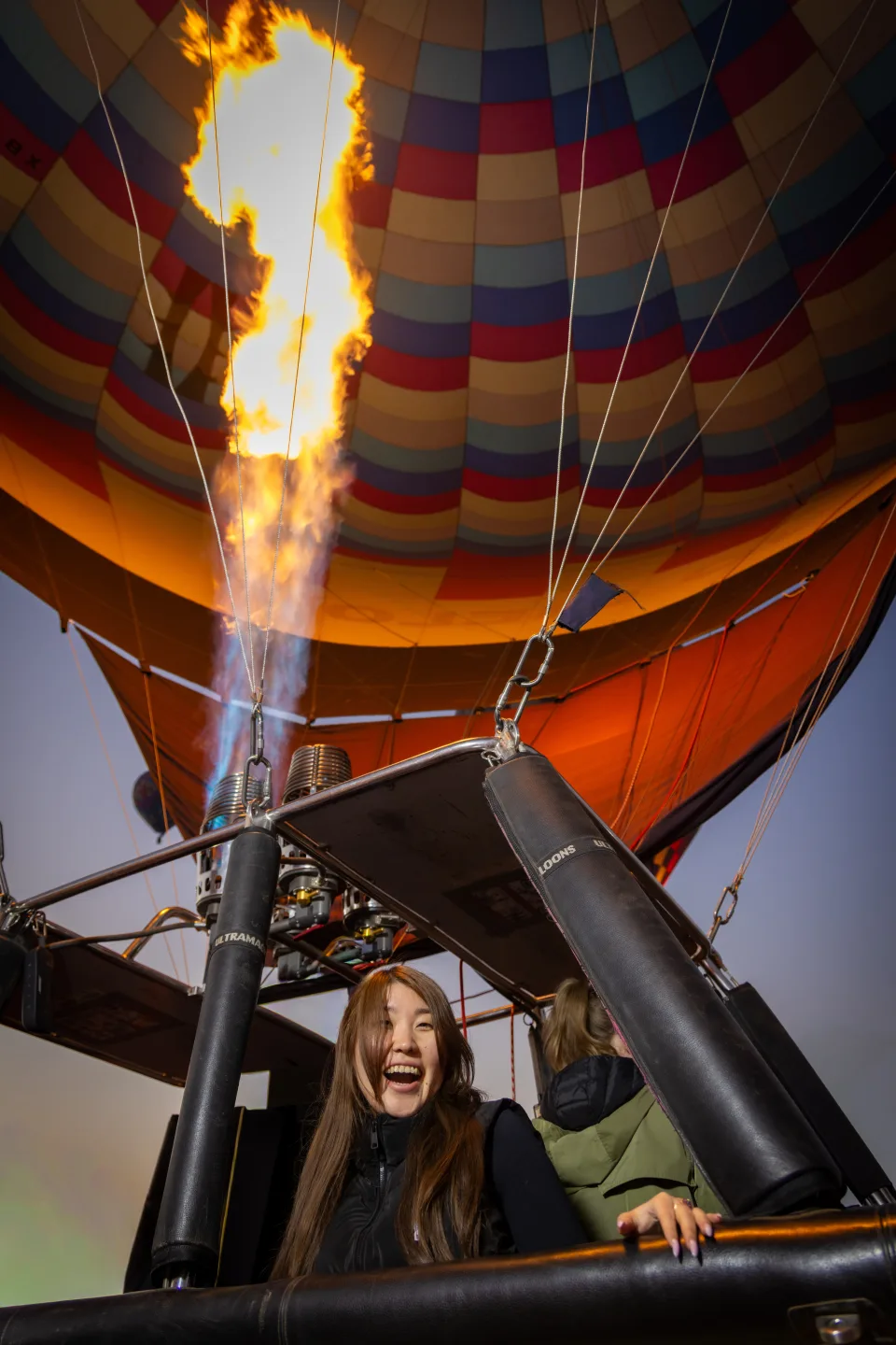 Laughing woman in the basket as a tall burner flame lights the hot air balloon at sunrise