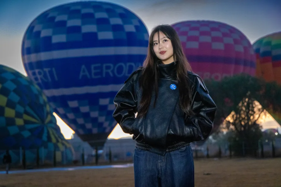 Woman in a leather jacket in front of a blue hot air balloon at dawn