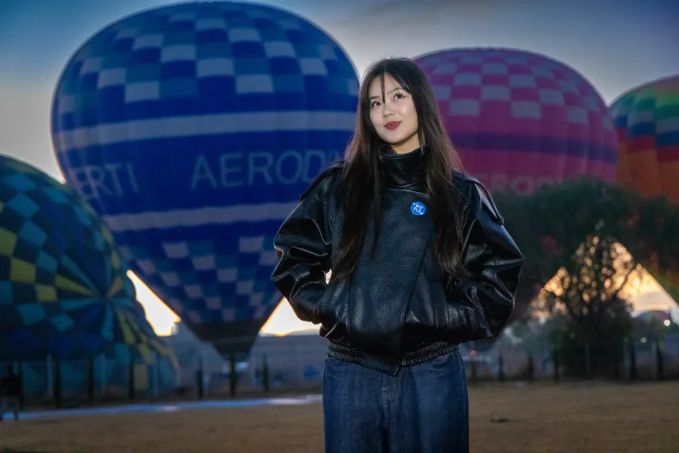 Woman posing before a blue hot air balloon in the launch field at dawn