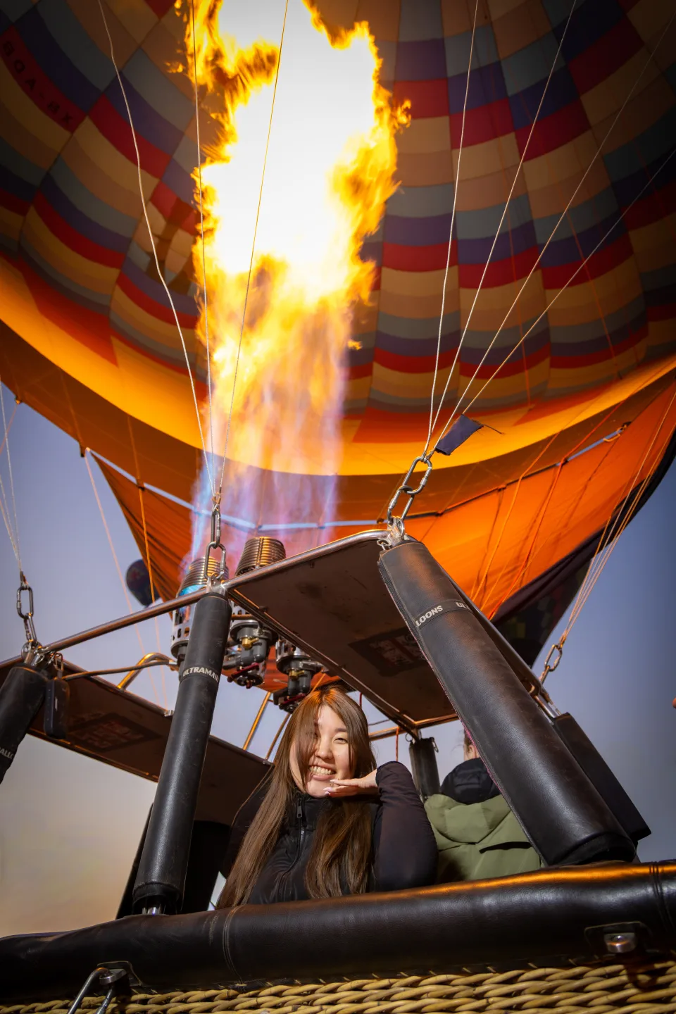 Woman posing in the basket beneath a powerful burner flame at sunrise