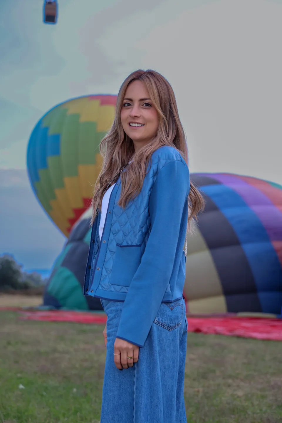 Woman in profile with hot air balloons in the launch field behind her at dawn