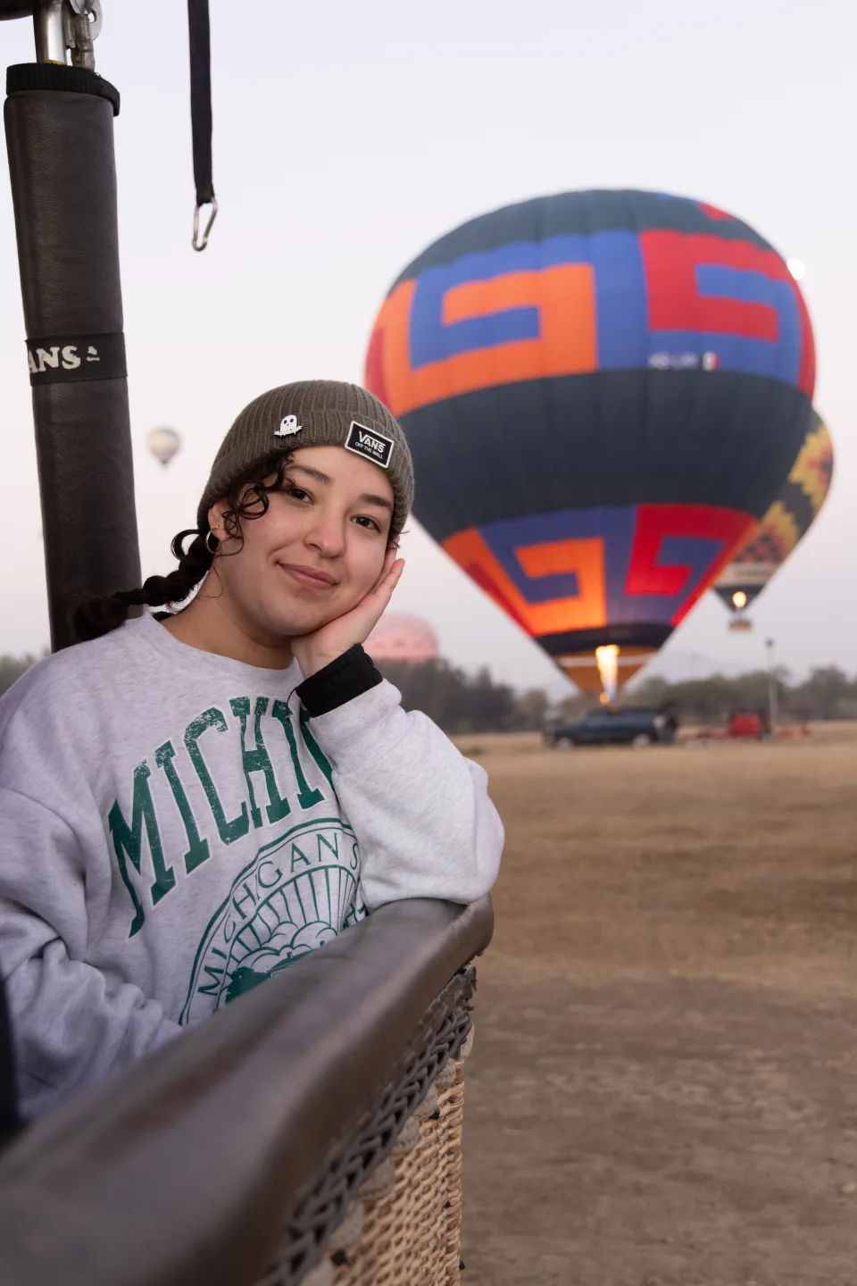 Woman resting her head on the balloon basket edge with a balloon on the field at dawn