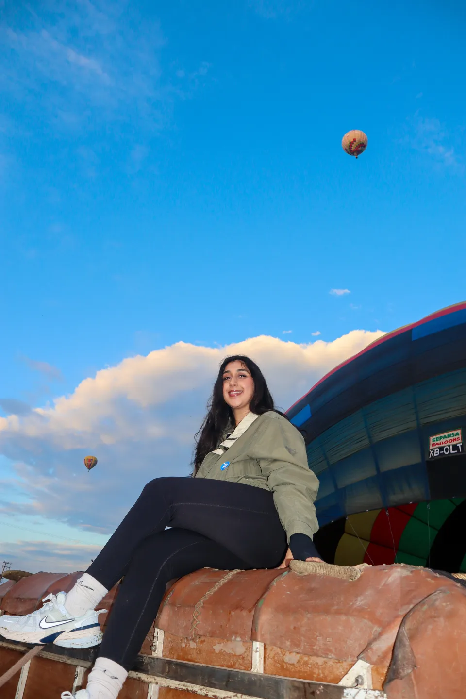 Woman sitting on a balloon basket with hot air balloons floating in a clear blue sky