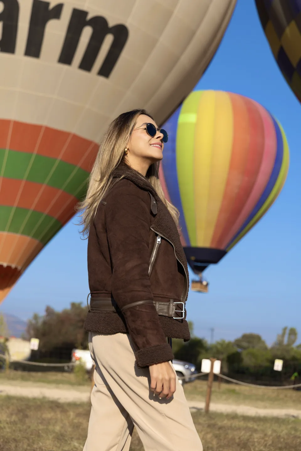 Woman in sunglasses walking past colorful hot air balloons under a blue sky