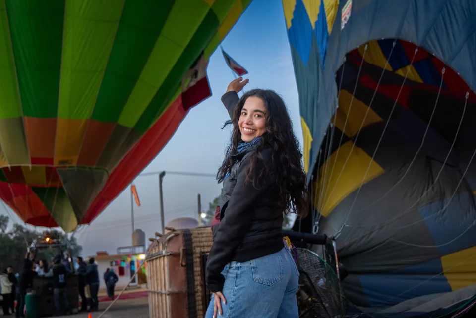 Smiling woman waving between two large inflating hot air balloons at dawn